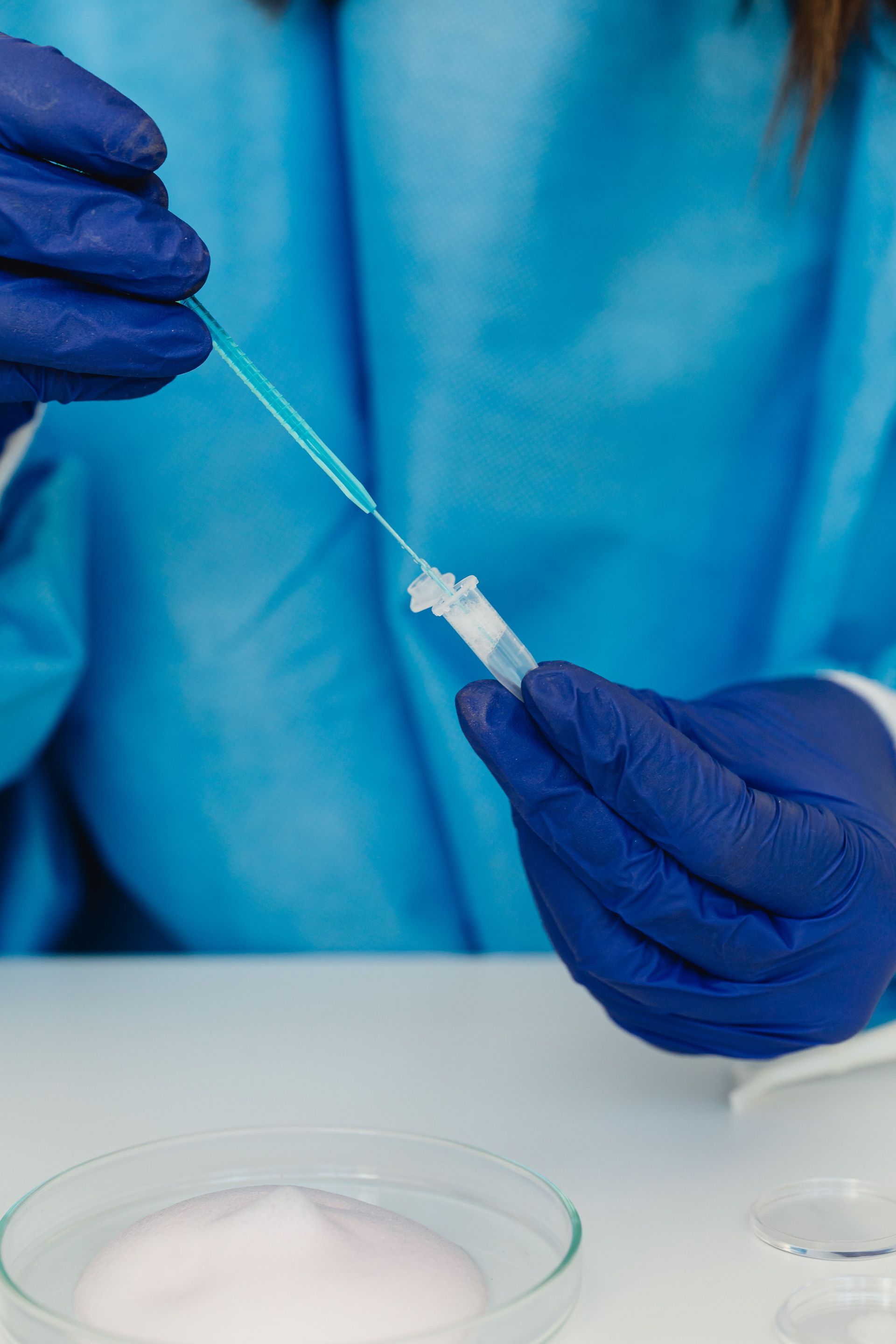 Close-up of a scientist handling a dropper with blue gloves in a lab environment.