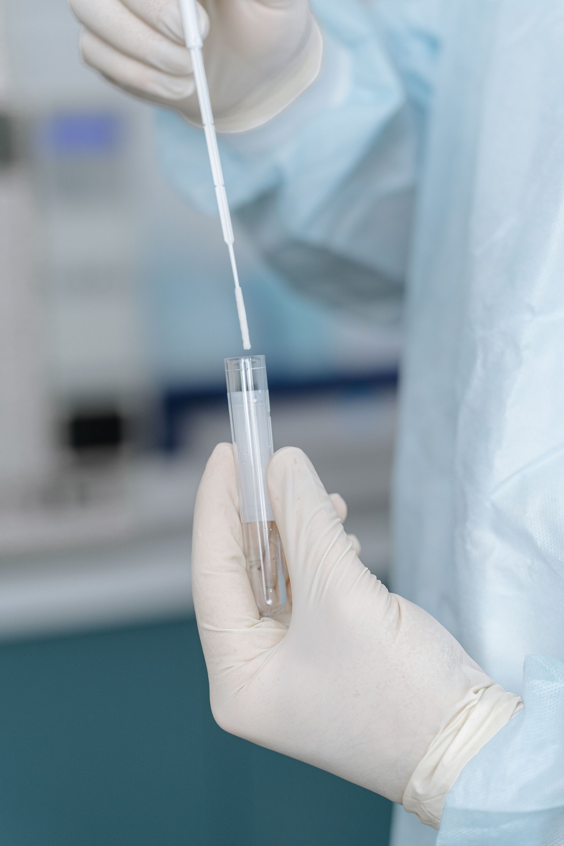 Close-up of scientist holding test tube and swab in laboratory setting, highlighting COVID-19 research.