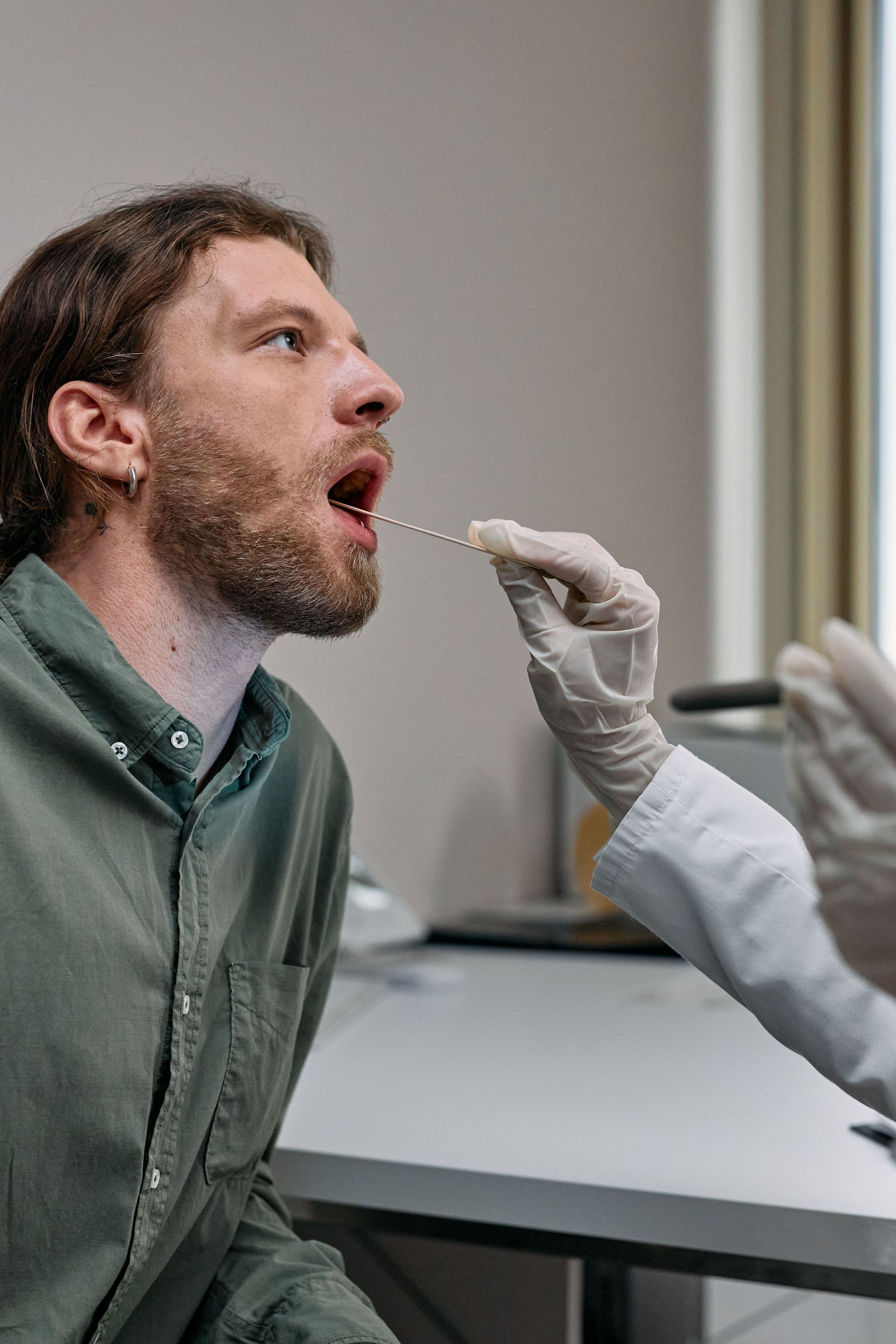 Healthcare worker administering a COVID-19 swab test to a male patient in a doctor's office.
