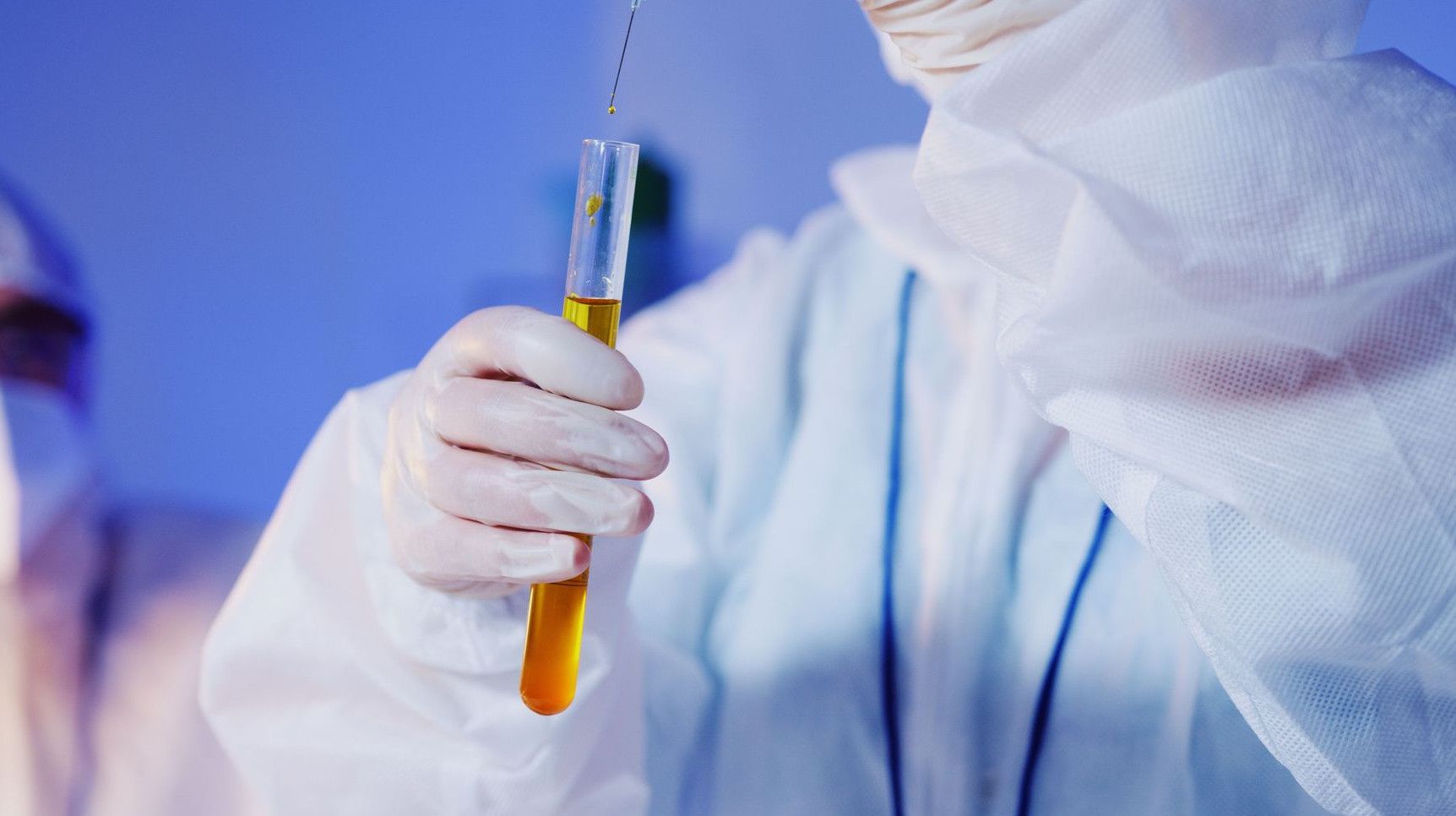 Scientist in protective gear conducting a test with a test tube in a laboratory setting.